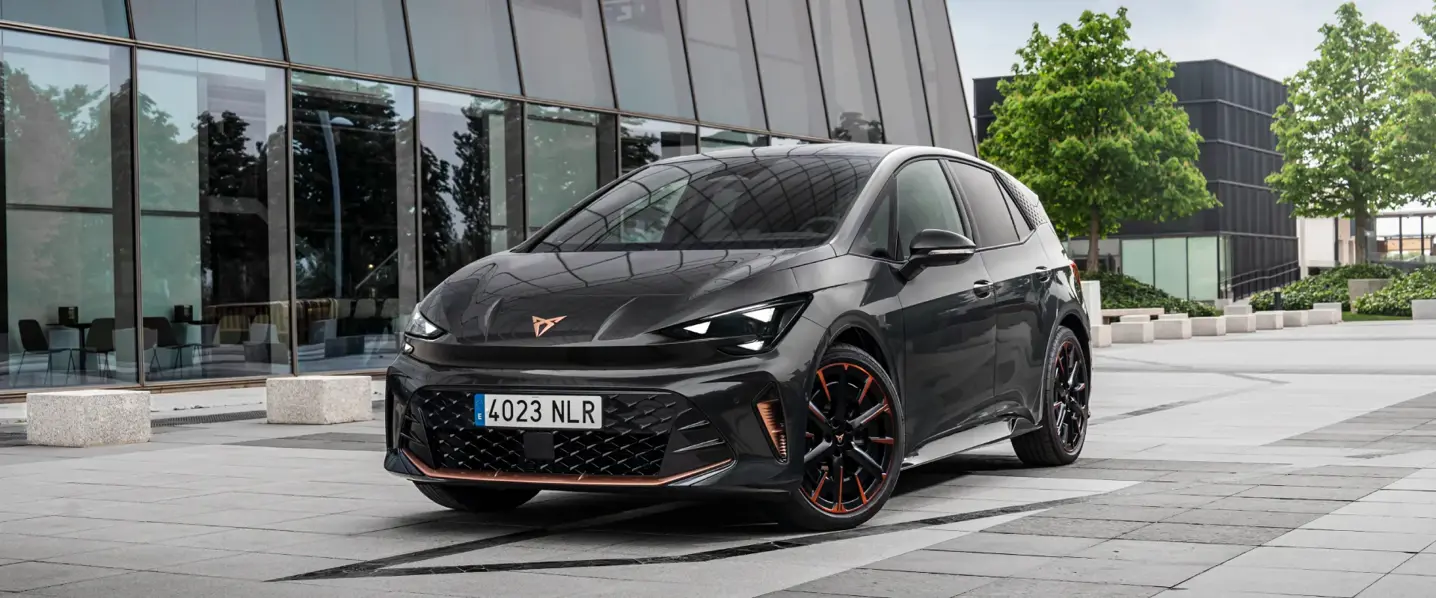 Sort, sporty elbil parkeret foran en moderne glasbygning i et bymiljø.